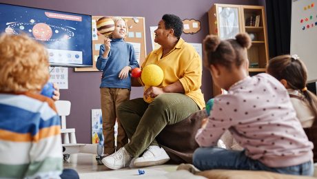 Cute little boy with Jupiter model standing by teacher at lesson